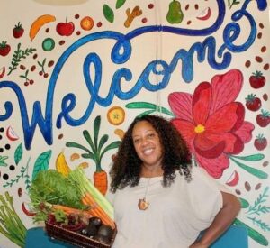 A woman, Bridgette Johnson, stands in front of a bright mural. 