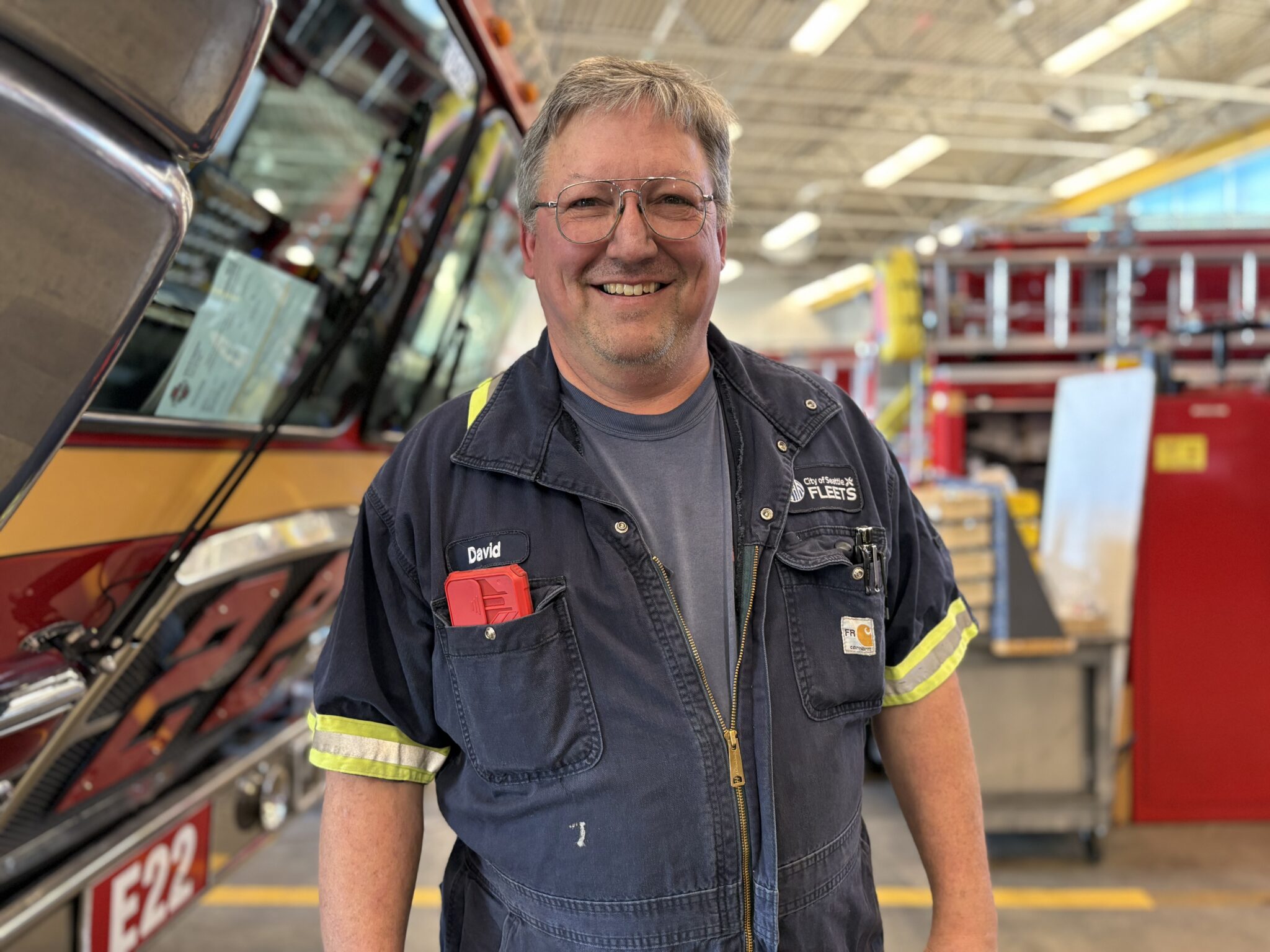 A man in a blue work suit stands in front of red fire trucks