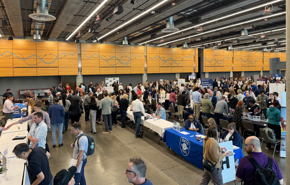 business owners attend the Reverse Vendor Trade Show inside the Fisher Pavilion at Seattle Center. Business owners speak with vendors at tables.